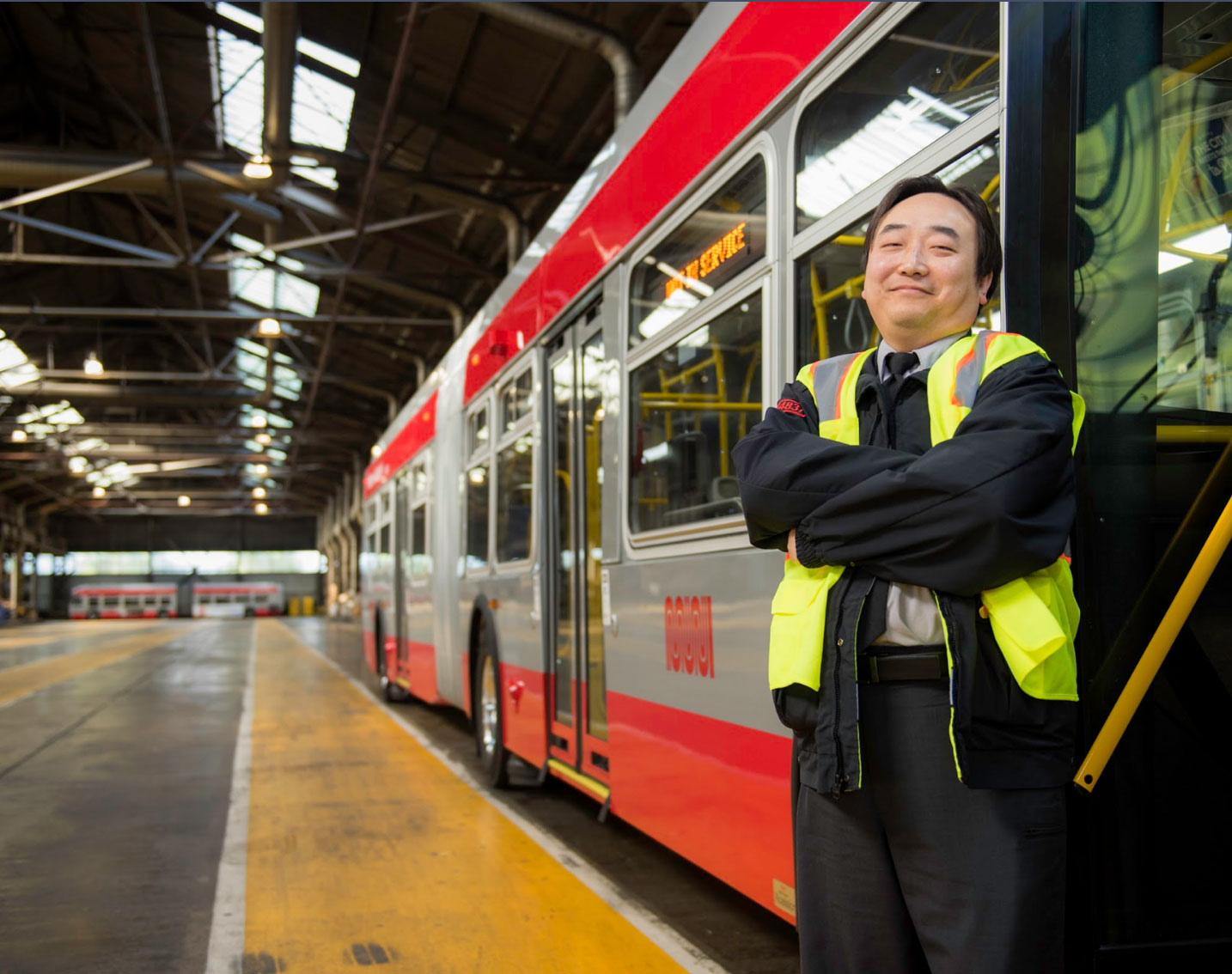 Smiling man in a safety jacket smiles at the camera, standing in front of the train.