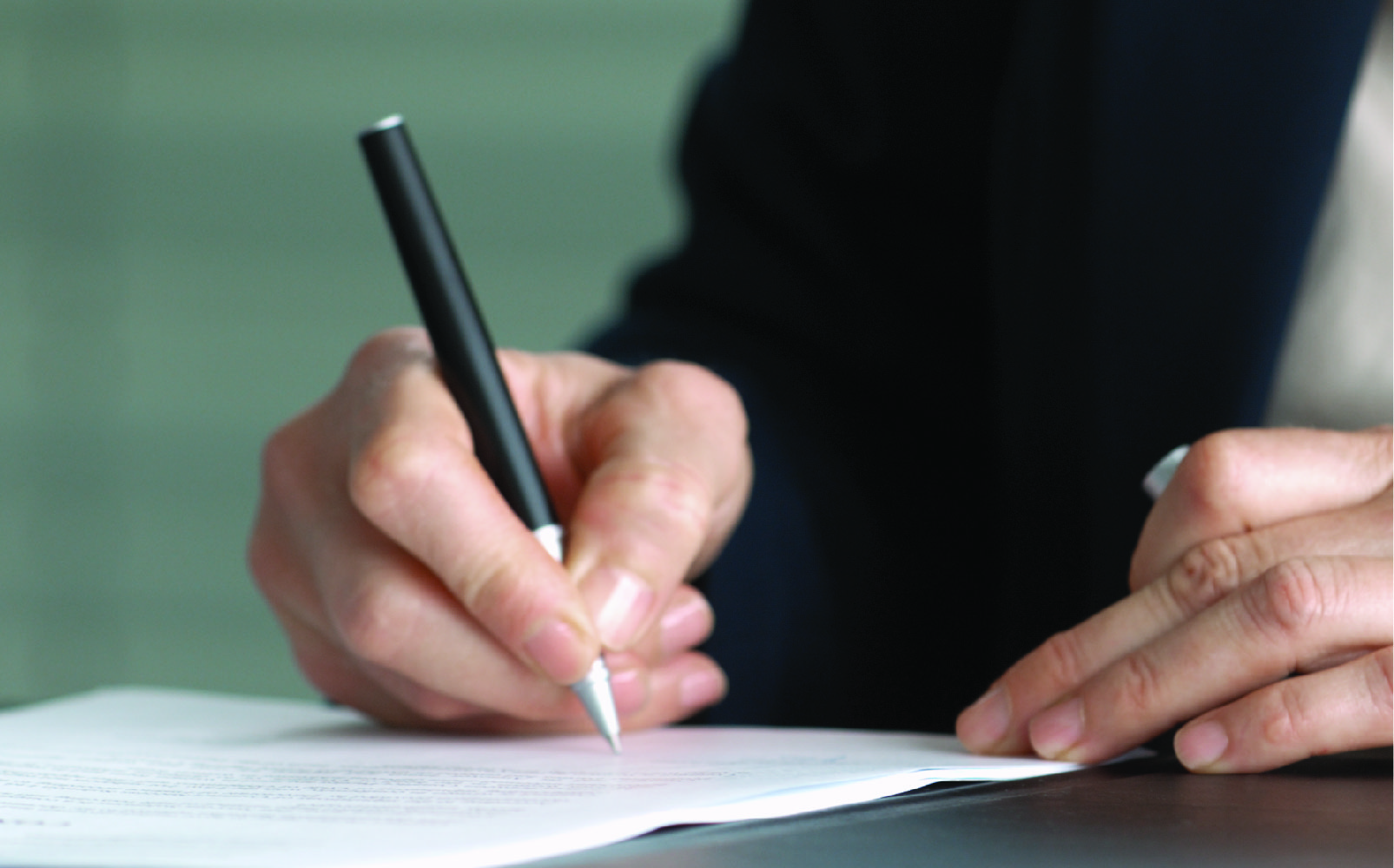 Photo of a woman's hand writing on a pad with a black pen.